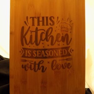 A wooden cutting board with the words " this kitchen is seasoned with love ".