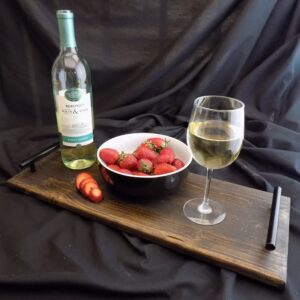 A bowl of strawberries next to a glass and bottle.